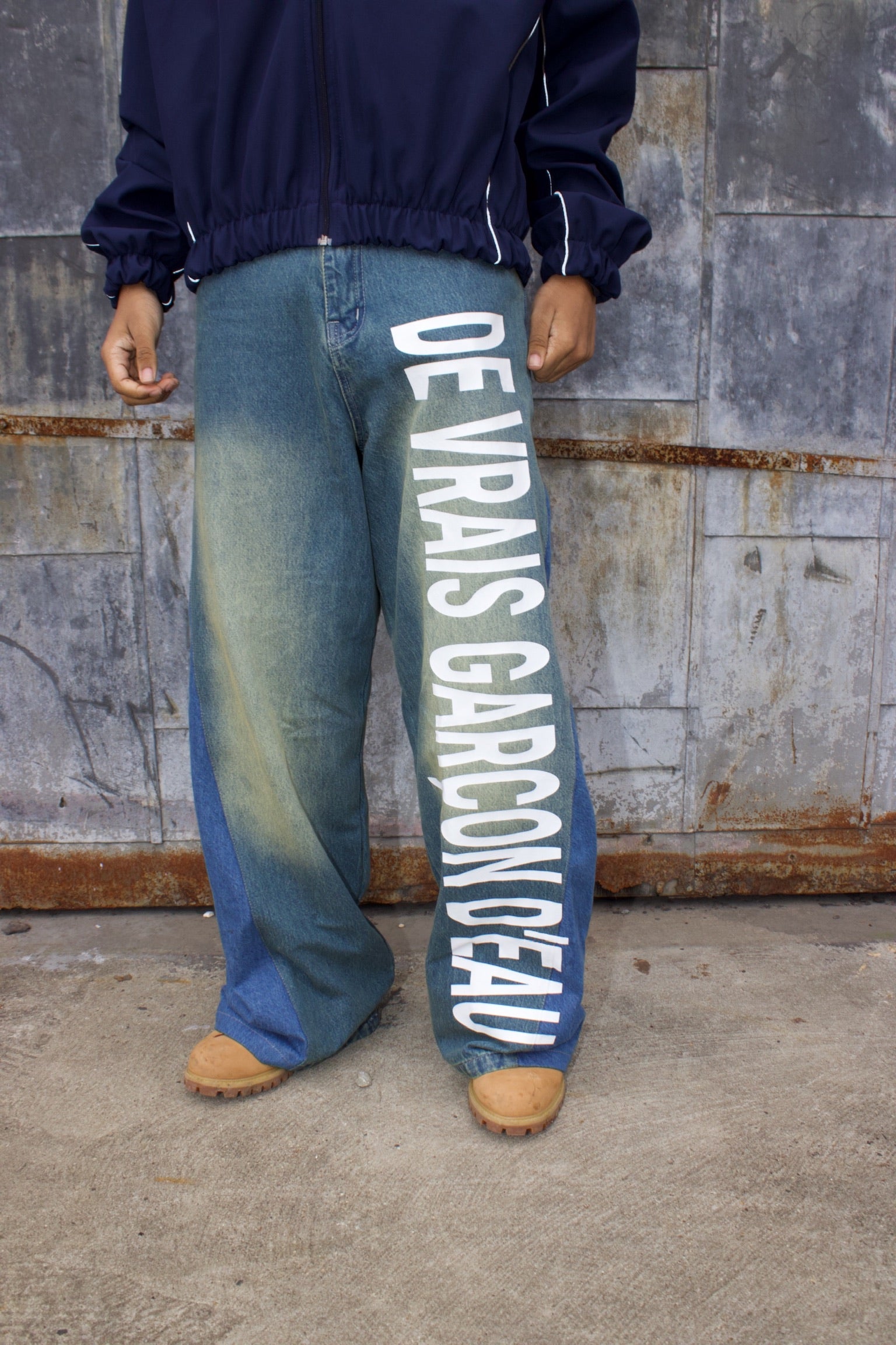 Person wearing blue jeans with white text against a textured wall.
