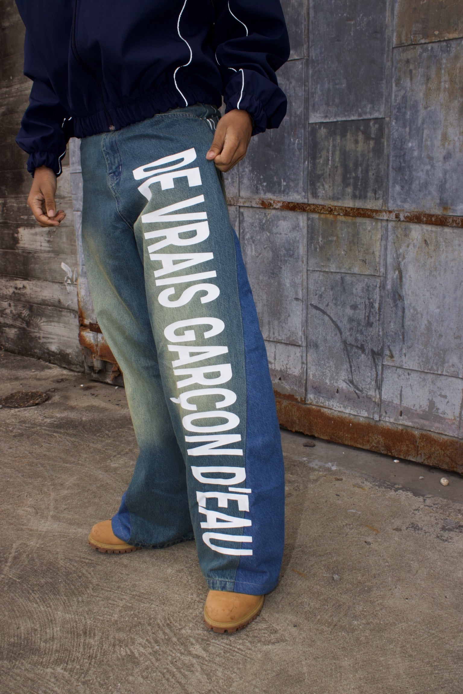 Person wearing blue jeans with white text standing against a textured wall.