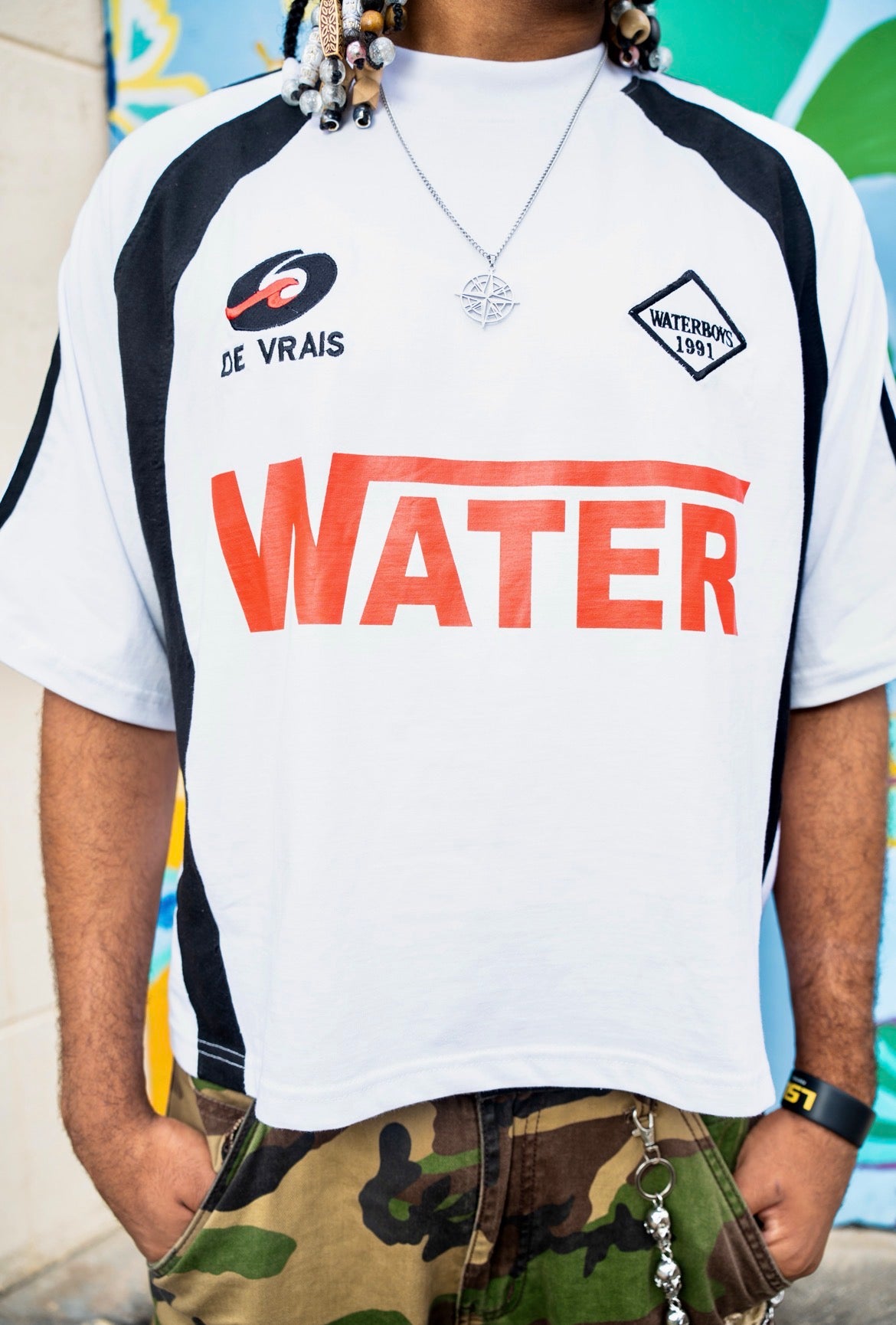 Person wearing a white t-shirt with 'WATER' printed on it, standing against a colorful mural.