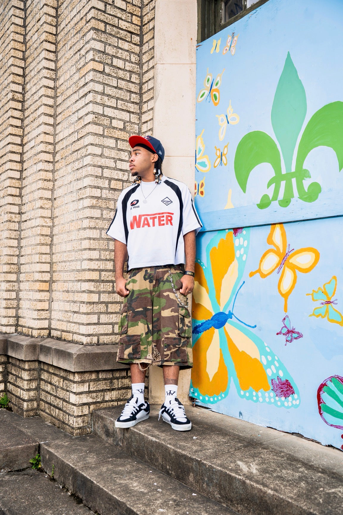 Person wearing a white t-shirt with 'WATER' printed on it, standing on steps next to a colorful mural.